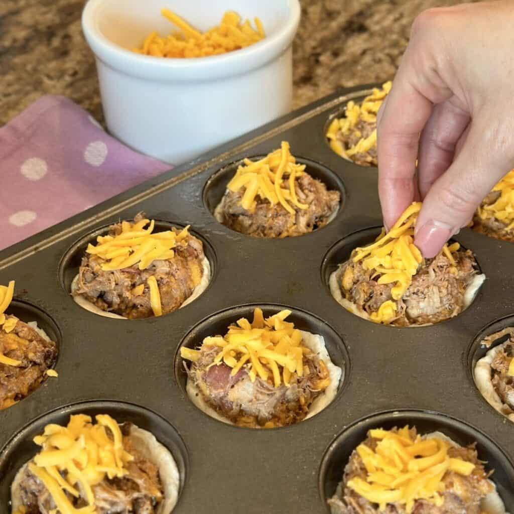 Adding cheese to the top of bbq biscuit cups.