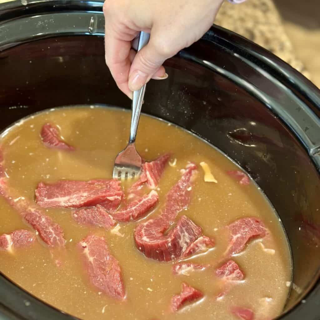 Mixing steak in liquid in a crockpot.