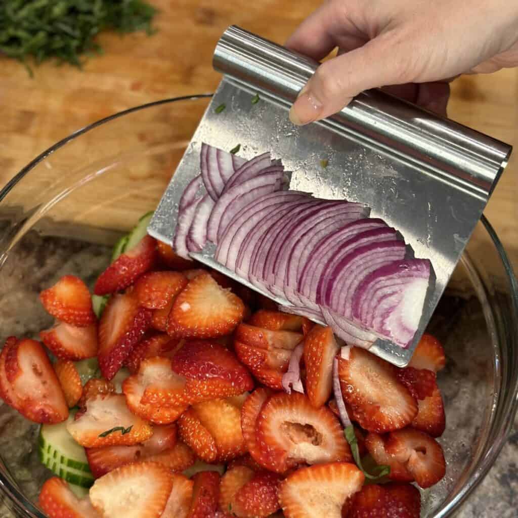 Adding red onion to a salad in a bowl.