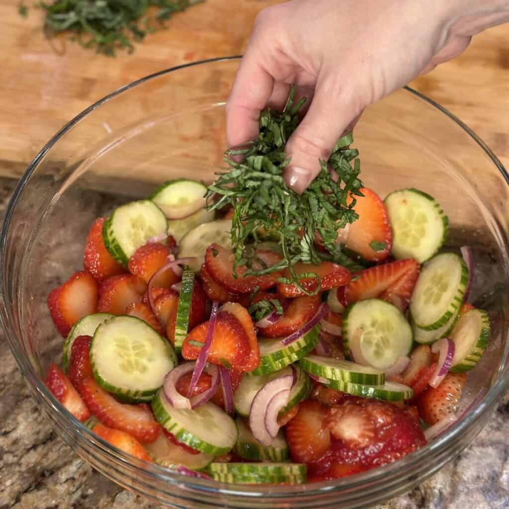 Adding basil and mint to a salad in a bowl.