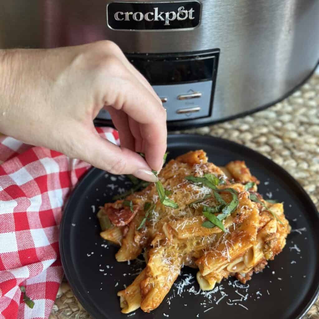 Adding basil to the top of crockpot pizza casserole.