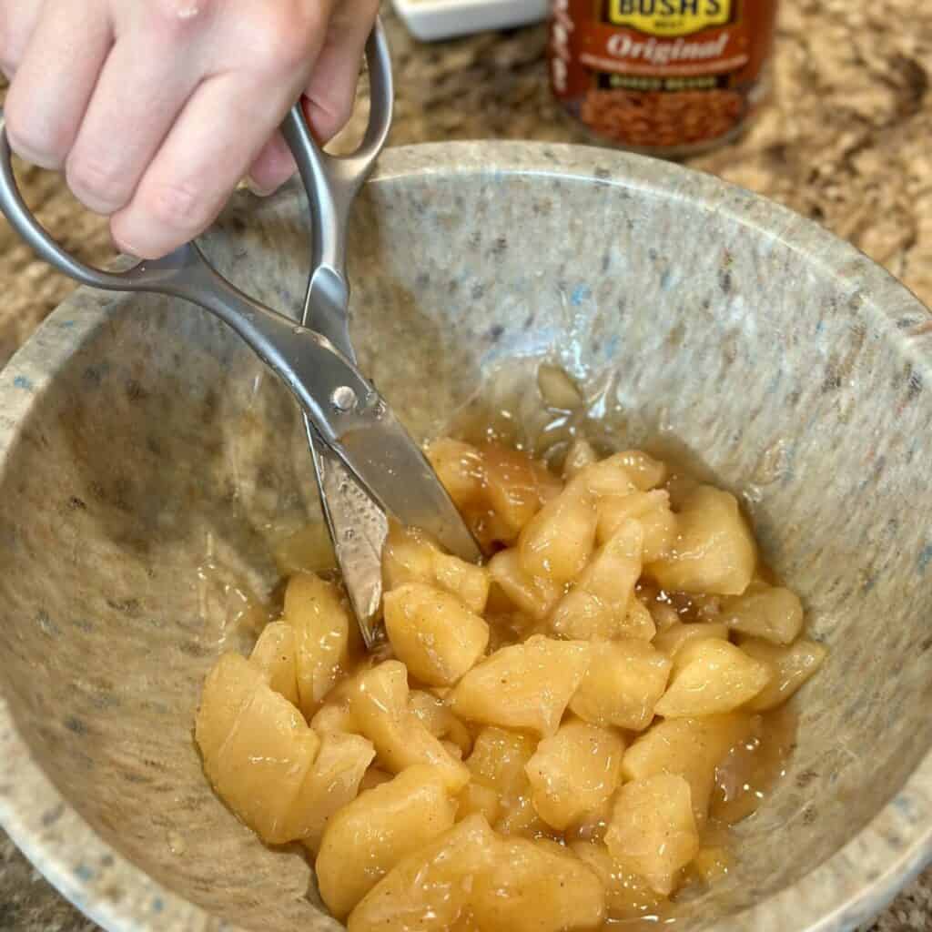 Cutting apples in a bowl with scissors.