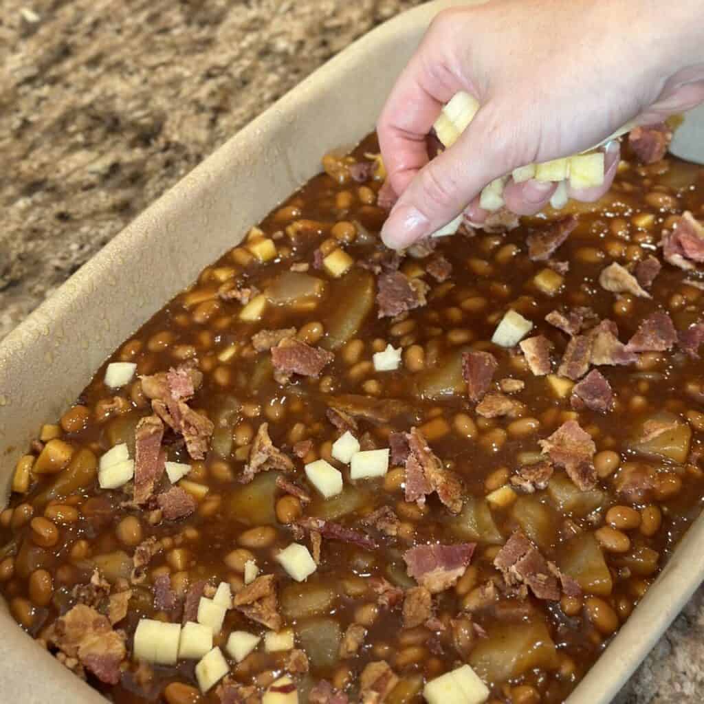 Adding chopped apple to the top of baked beans.