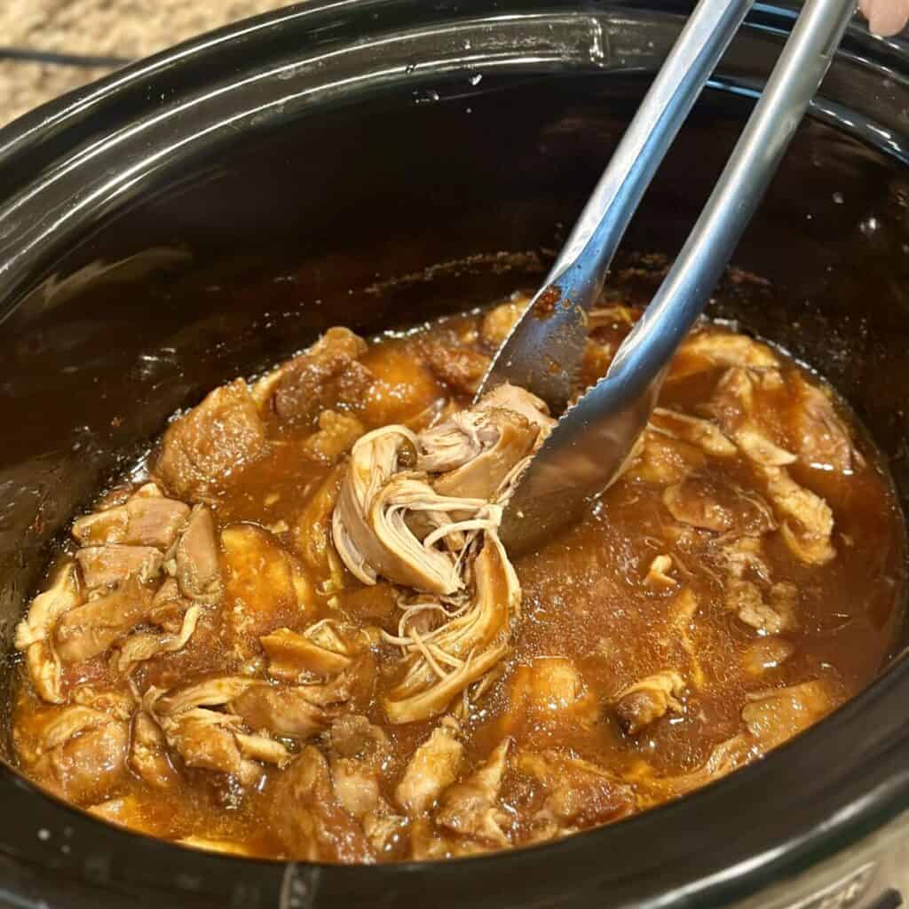 Adding cooked chicken to sauce in a crockpot.