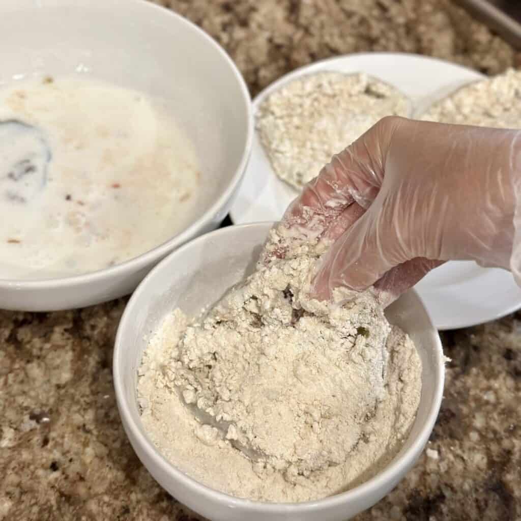 Coating a green tomato in a flour mixture.