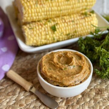 A bowl of cajun butter next to corn.