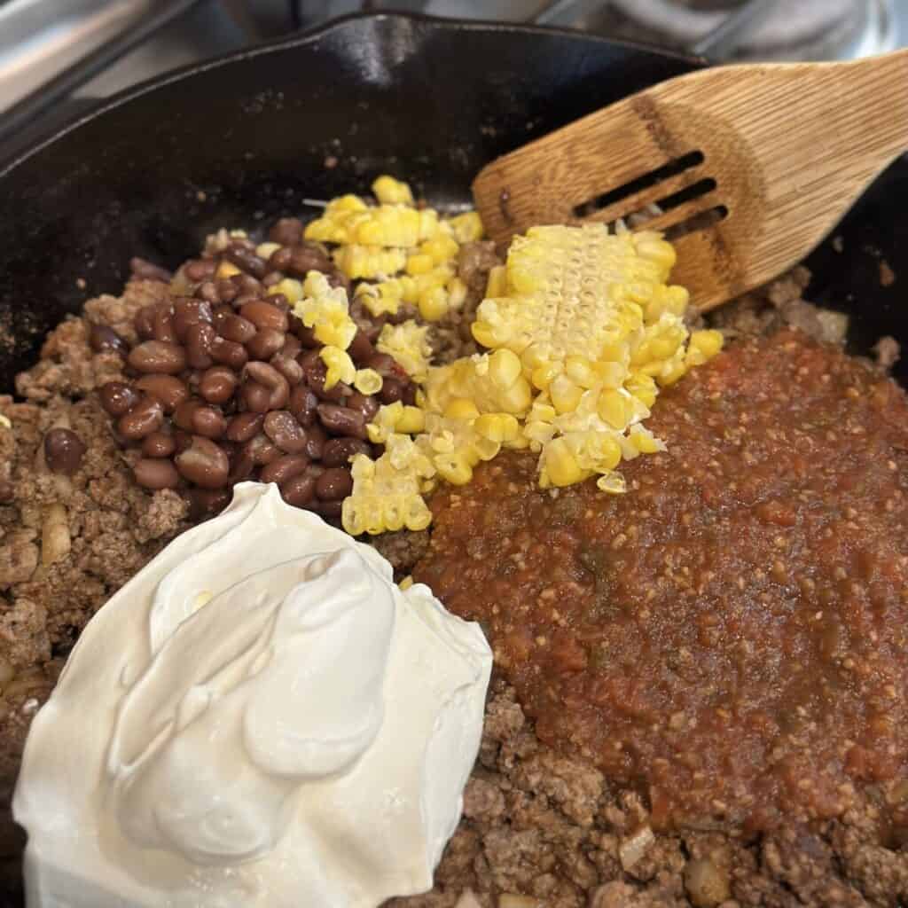 Adding corn, salsa and sour cream in ground beef.