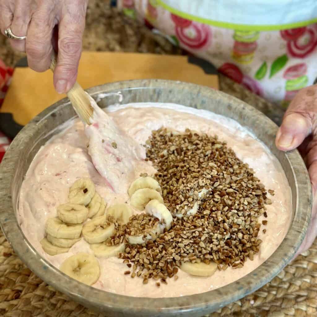 Folding bananas and pecans in a frozen fruit salad.