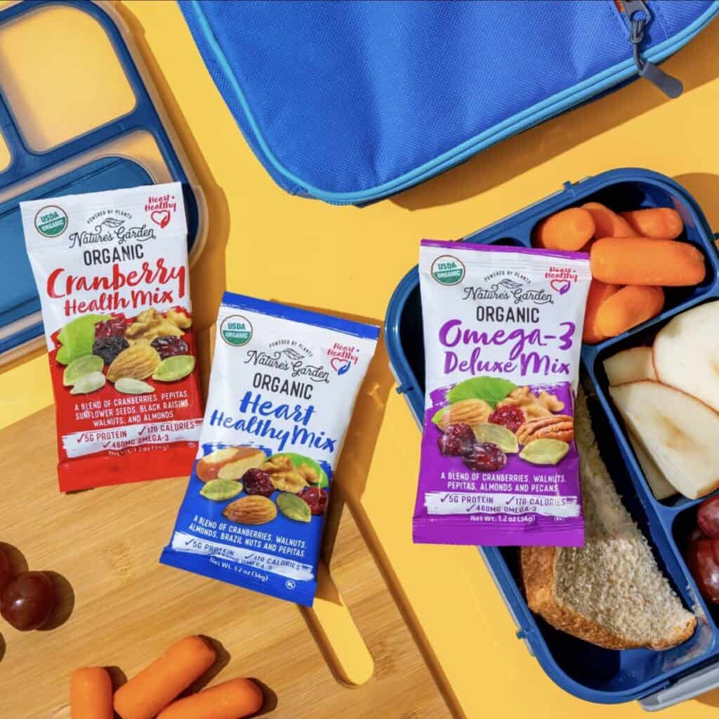 Three packs of trail mix snacks mixes next to a lunch box.