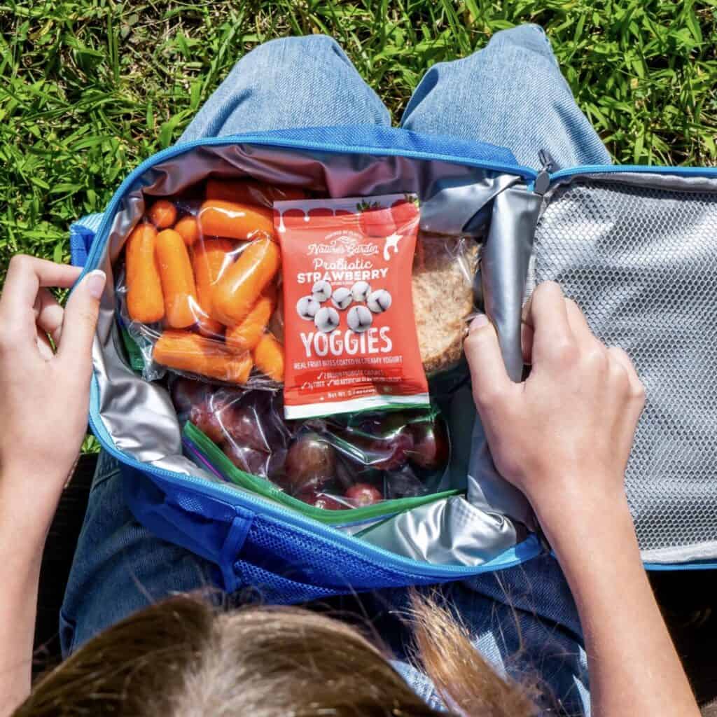 A kid holding an opened lunchbox with healthy snacks for kids inside.