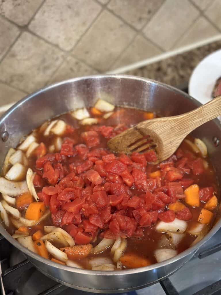 Adding tomatoes to a swiss steak gravy.