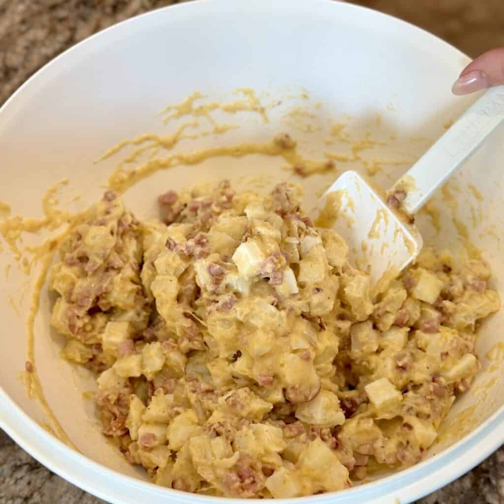 Mixing cubed potatoes with cheese sauce.