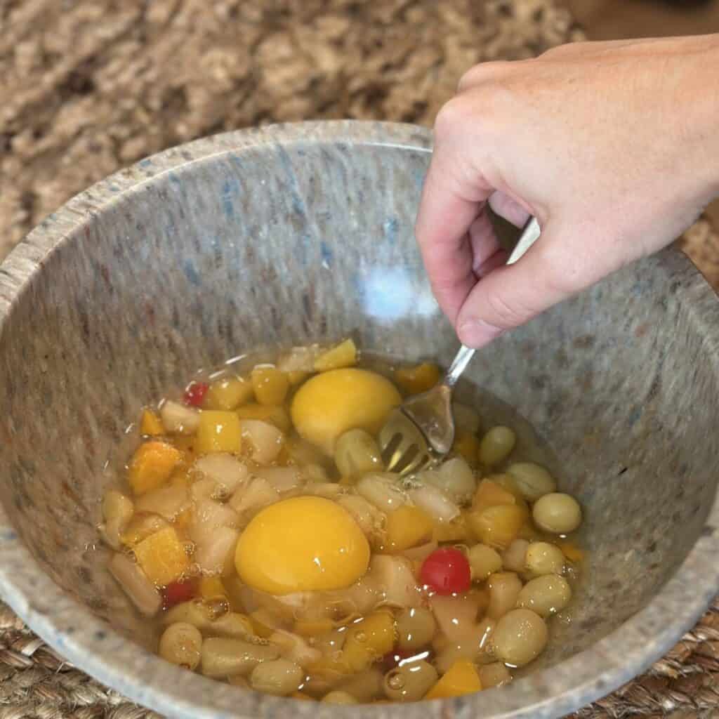 Mixing together fruit cocktail and eggs in a bowl.