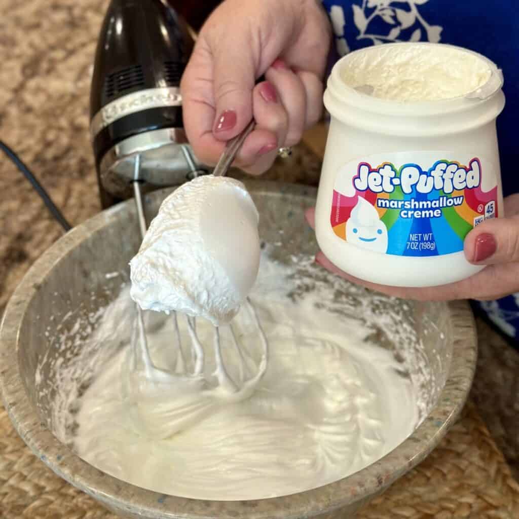 Adding marshmallow cream to egg whites in a bowl.