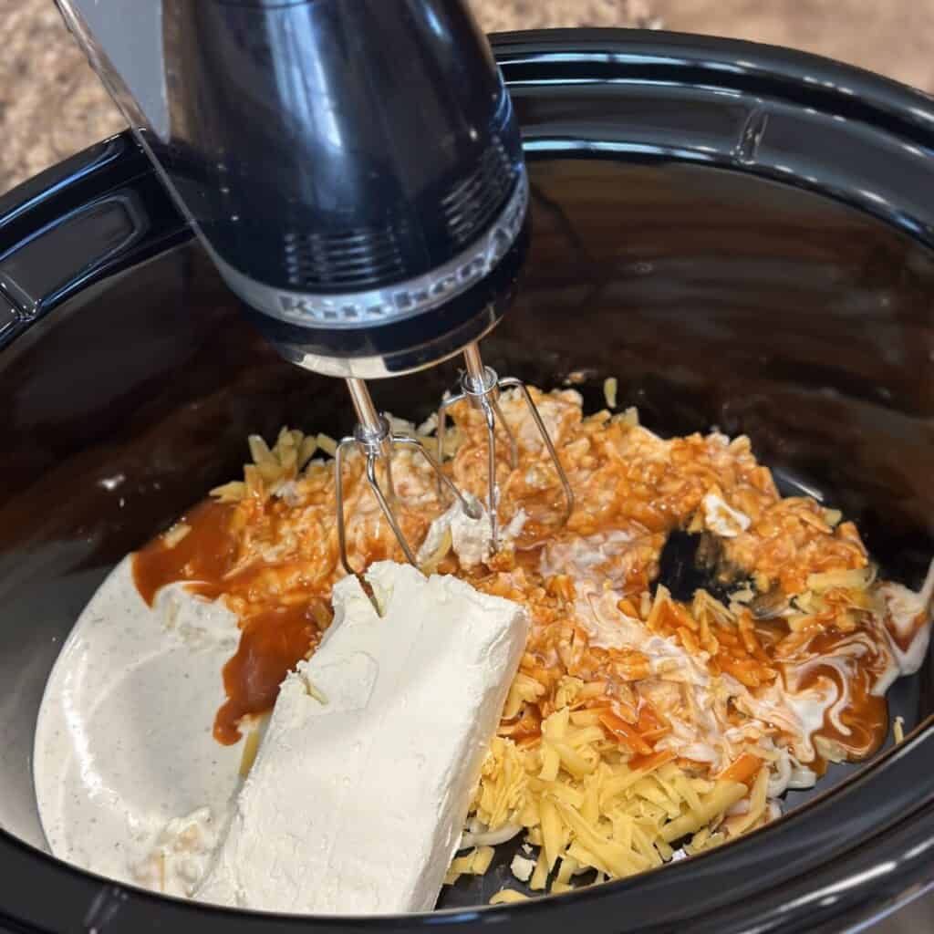 Blending together buffalo chicken dip in a slow cooker.