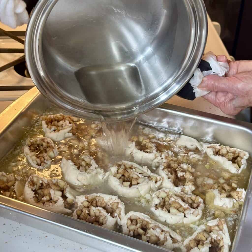 Pouring syrup on an apple roll in a pan.