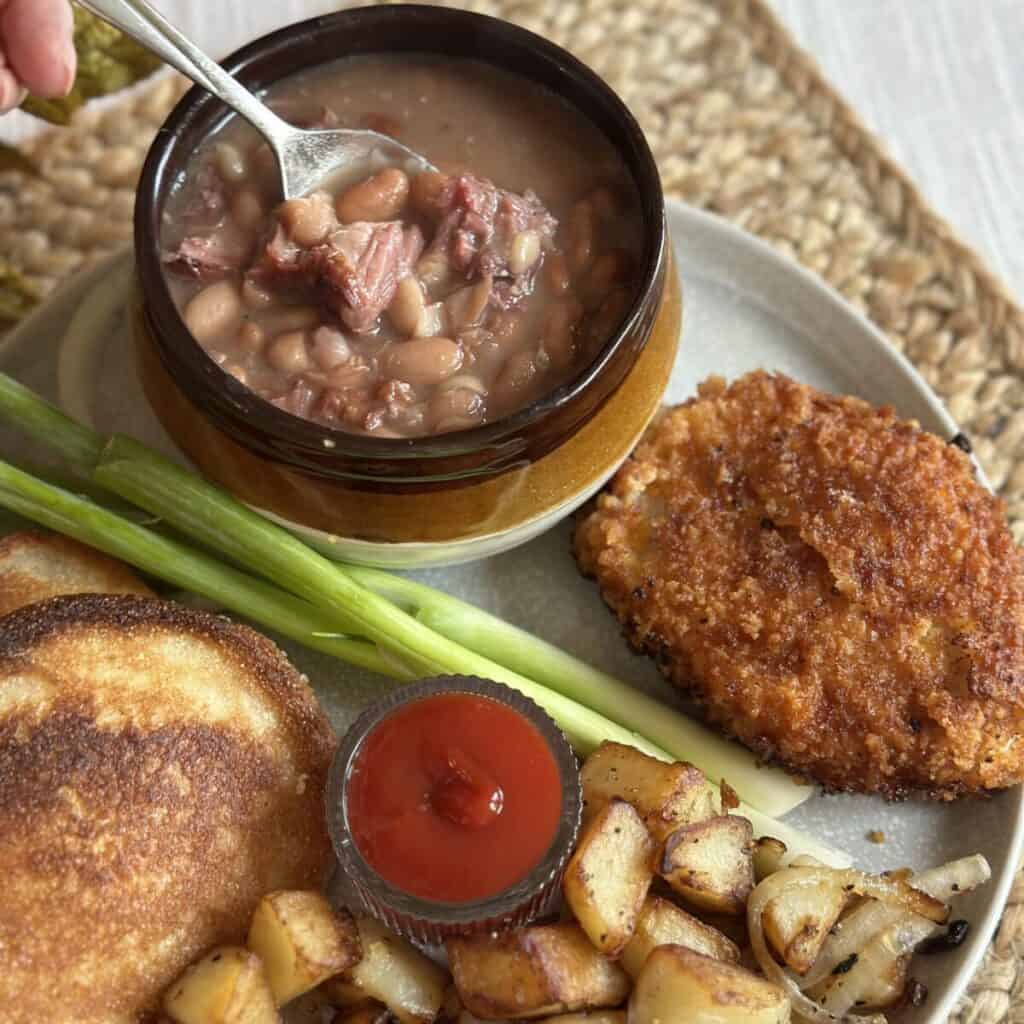 A plate with soup beans, hoecakes, fried potatoes and a fried pork chop.