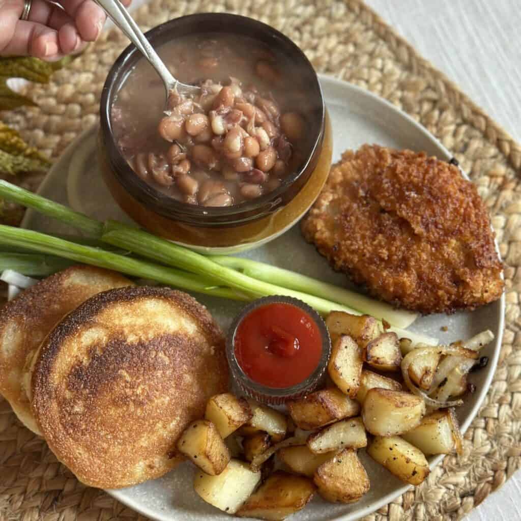 A plate with soup beans, hoecakes, fried potatoes and a fried pork chop.