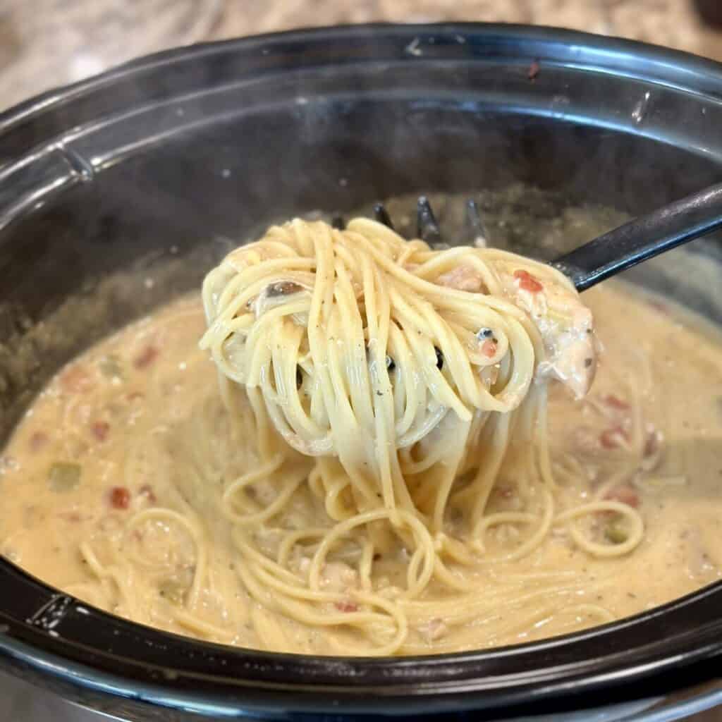 Stirring cooked spaghetti in sauce in a crockpot.