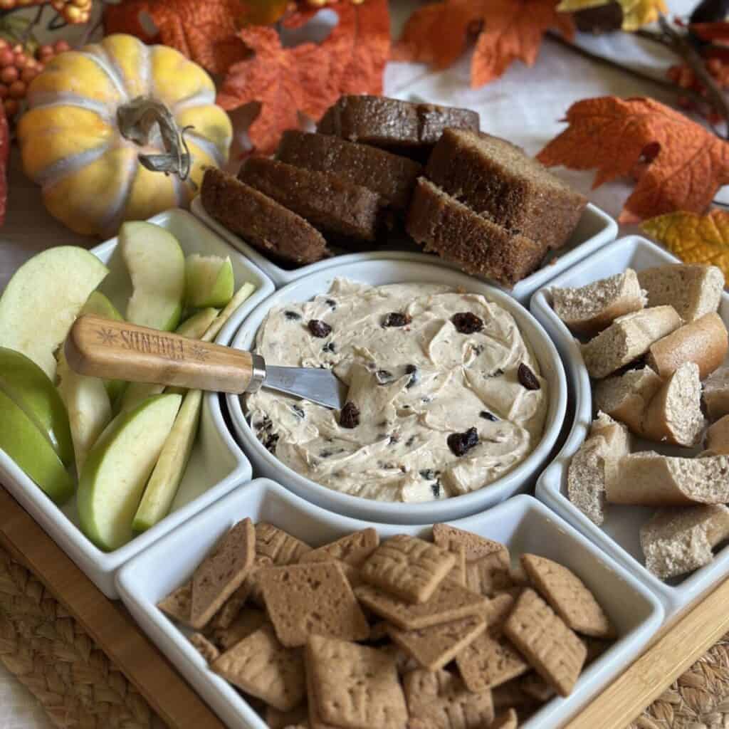 A tray of cinnamon cream cheese spread, apples, bread, crackers and bagels.