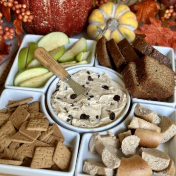 A tray of cinnamon cream cheese spread, apples, bread, crackers and bagels.