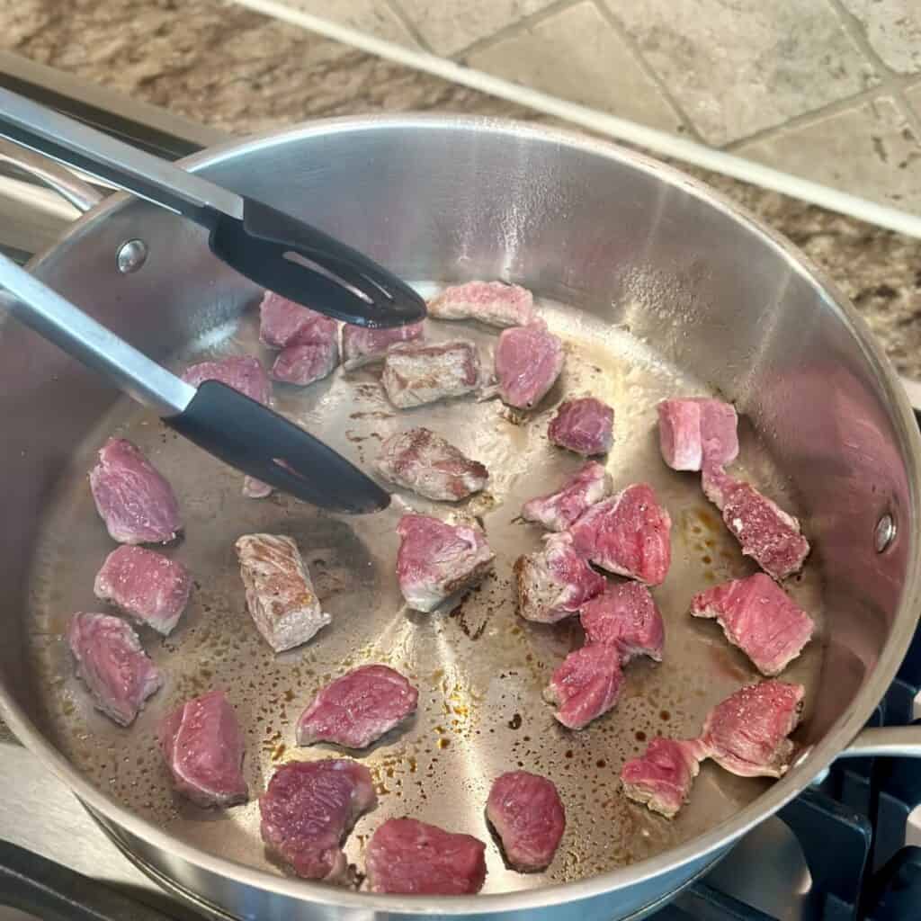 Searing beef chunks in a pan.