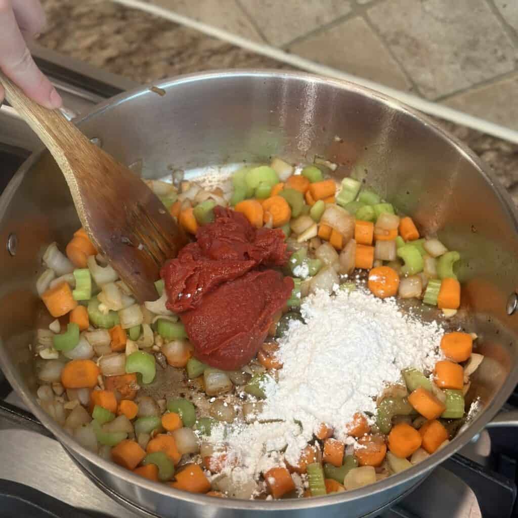 Adding tomato paste and flour to a pan of vegetables.