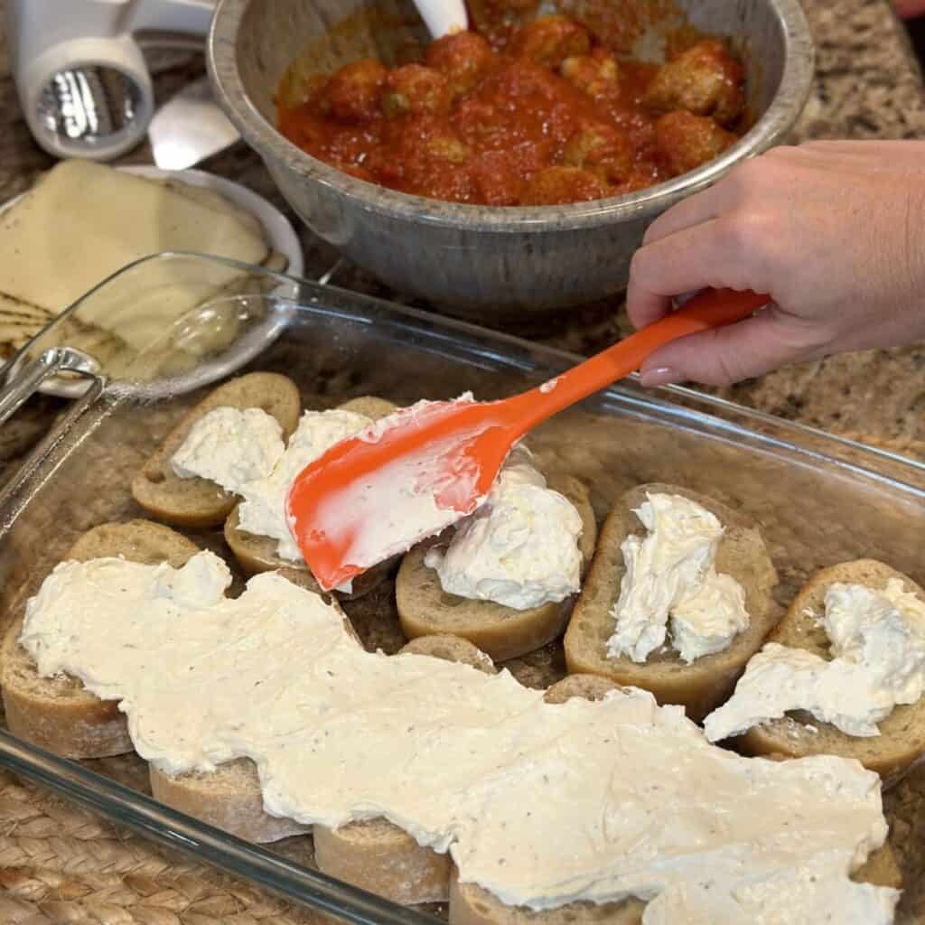 Spreading a cream cheese mixture on bread in a baking dish.