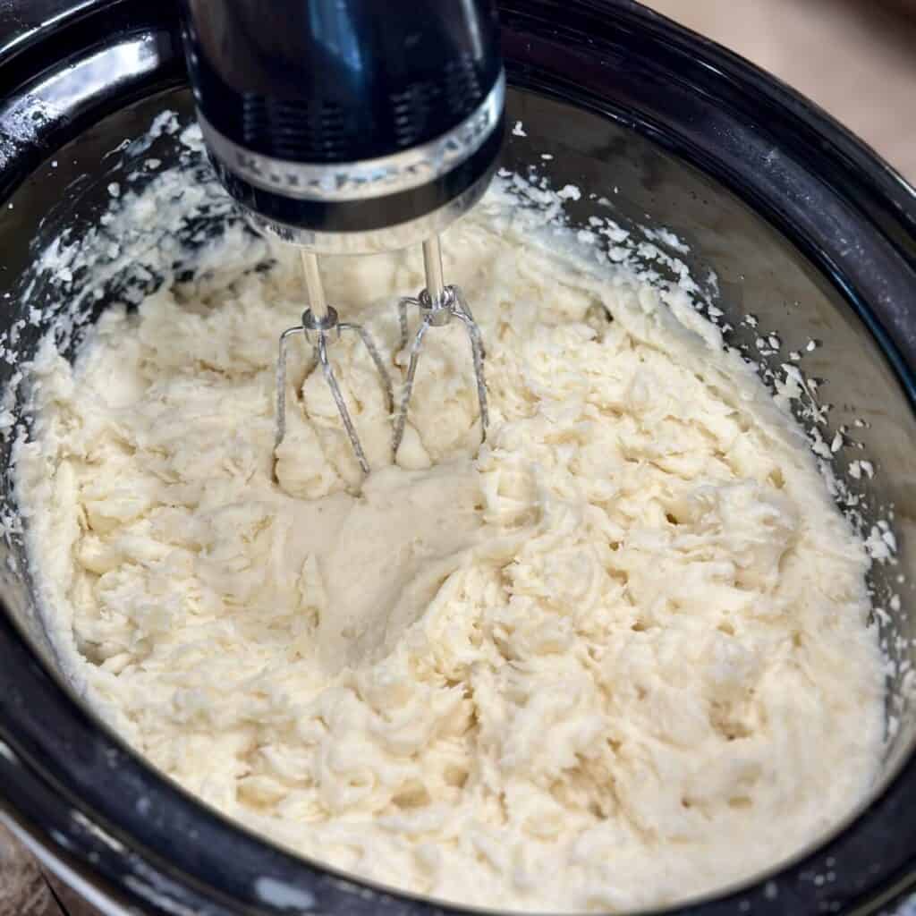 Whipping potatoes in a crockpot with a mixer.