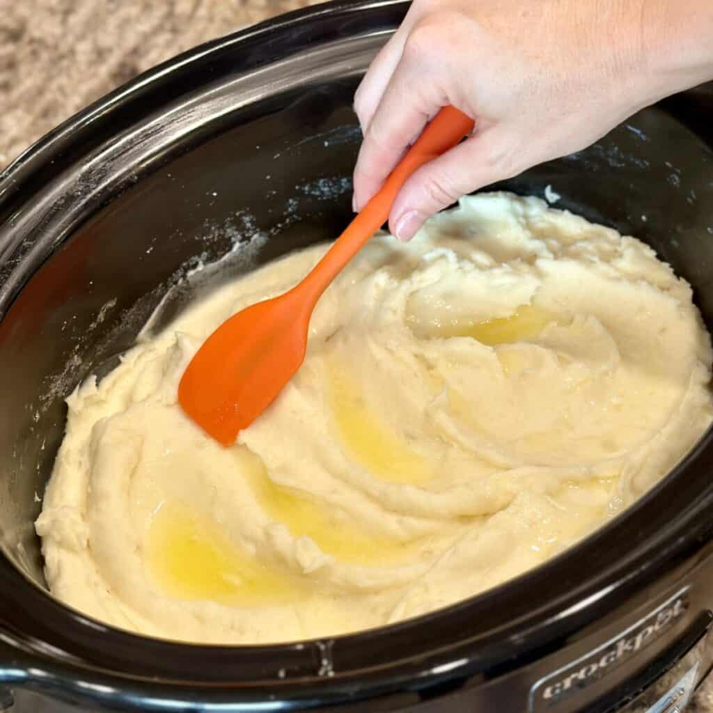 Spreading crockpot mashed potatoes in a single layer in a crockpot.