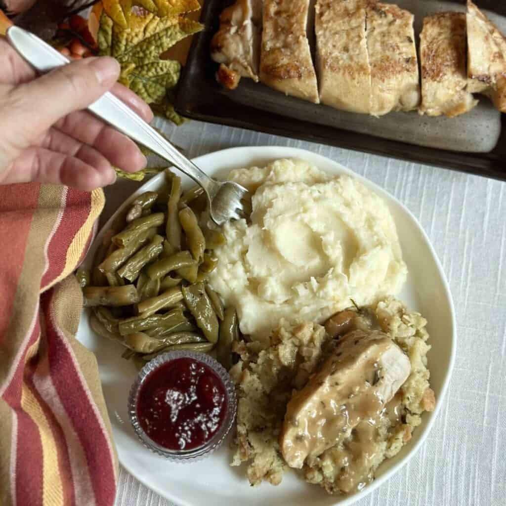 A plate with mashed potatoes, turkey, dressing and green beans. 