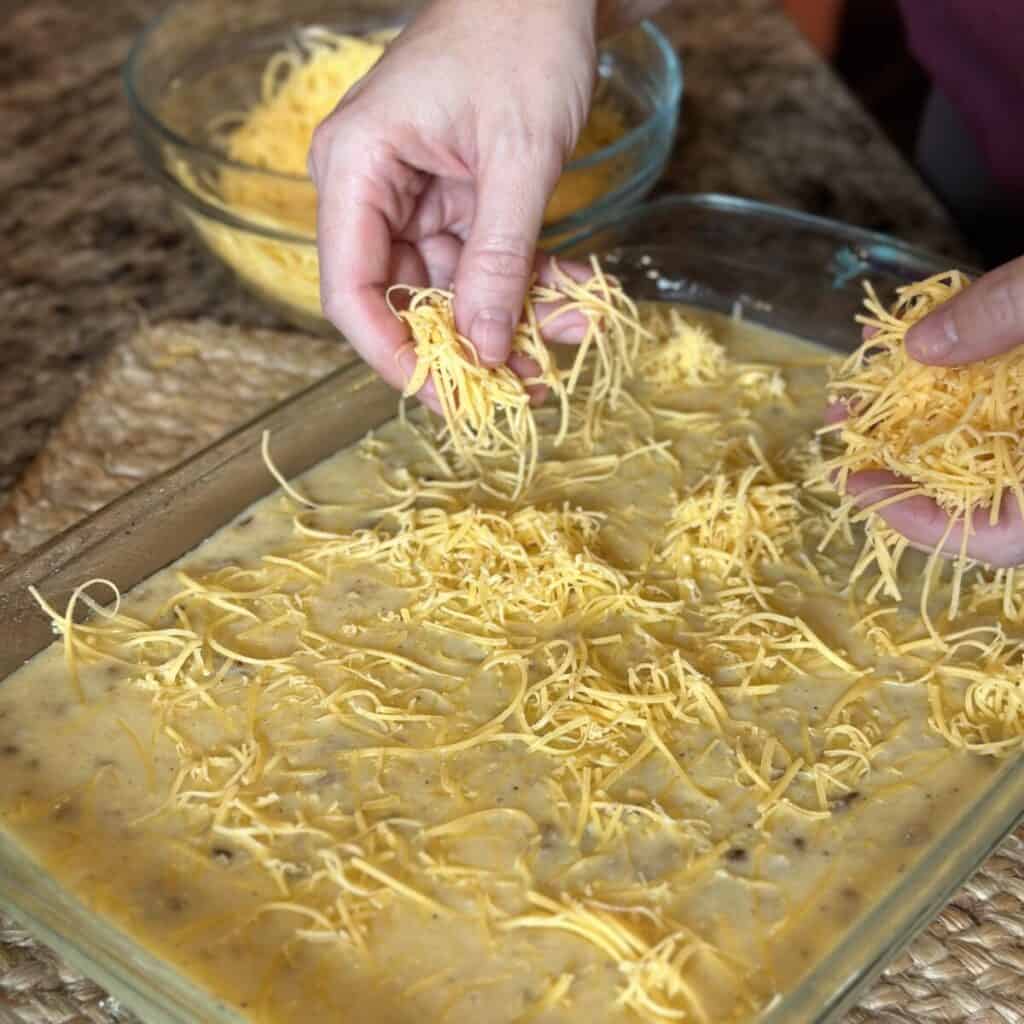 Adding cheese to the top of grits in a pan.