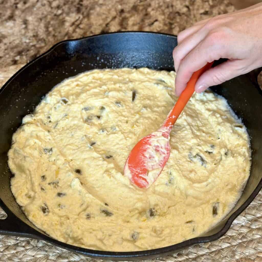 Spreading cornbread batter in a cast iron skillet.