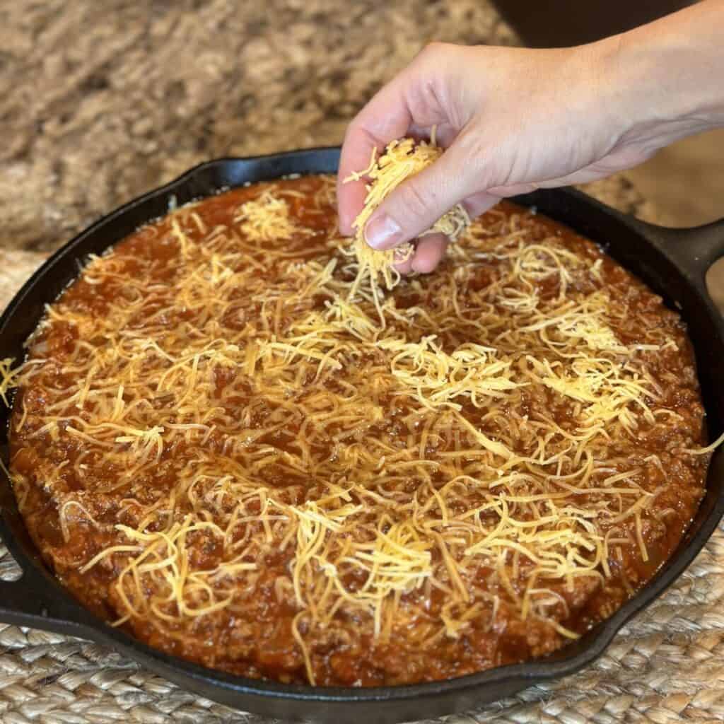 Adding cheese to the top of chili in a skillet.