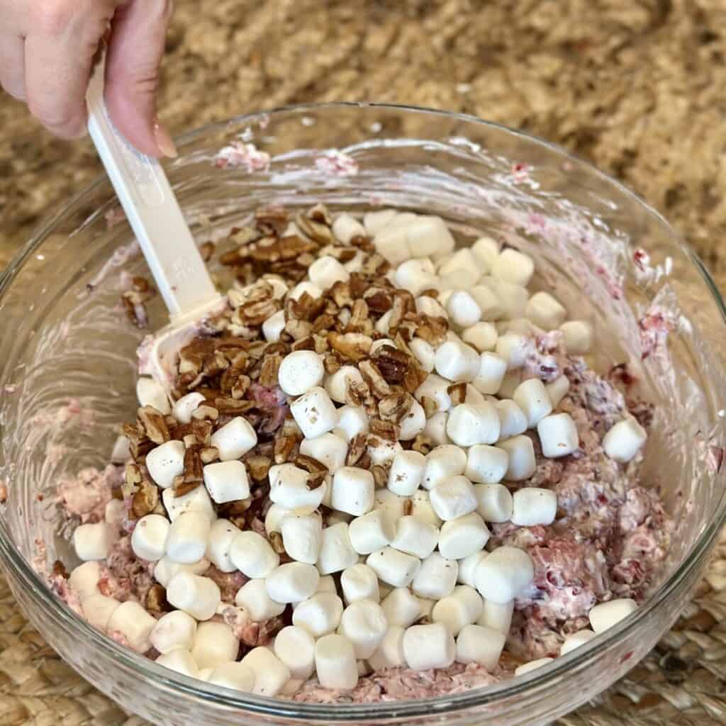 Adding marshmallows and pecans to a salad.