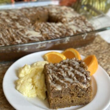 A slice of pumpkin coffee cake on a plate with eggs and orange slices.