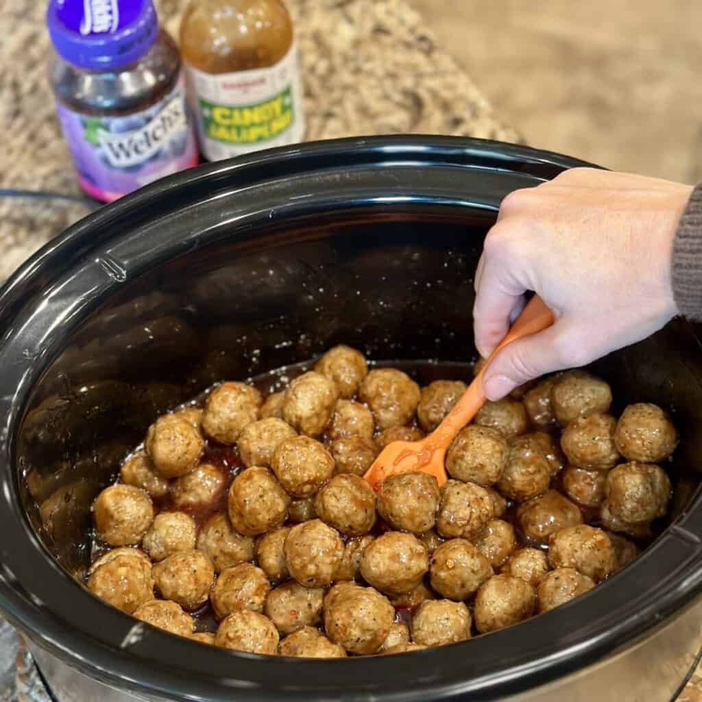 Folding meatballs in a grape jelly bbq sauce in a crockpot.