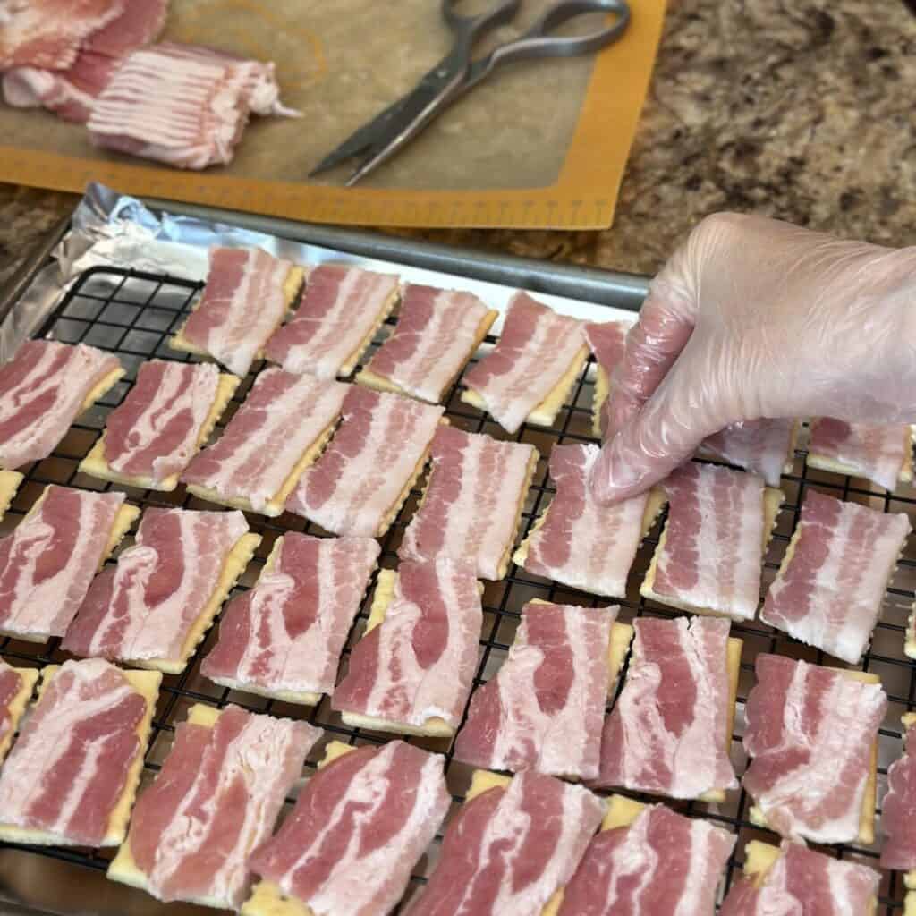 Laying bacon on crackers on a sheet pan.