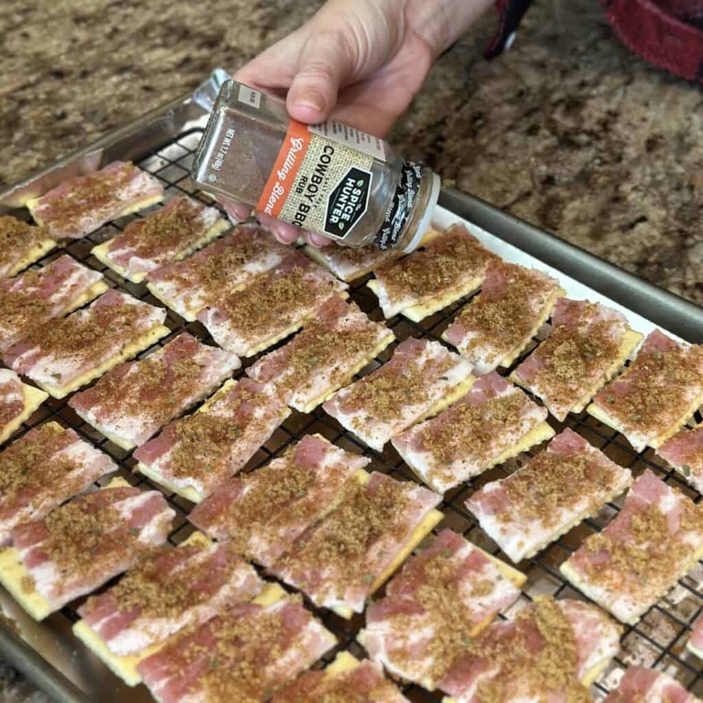 Sprinkling barbecue seasoning on bacon crackers.