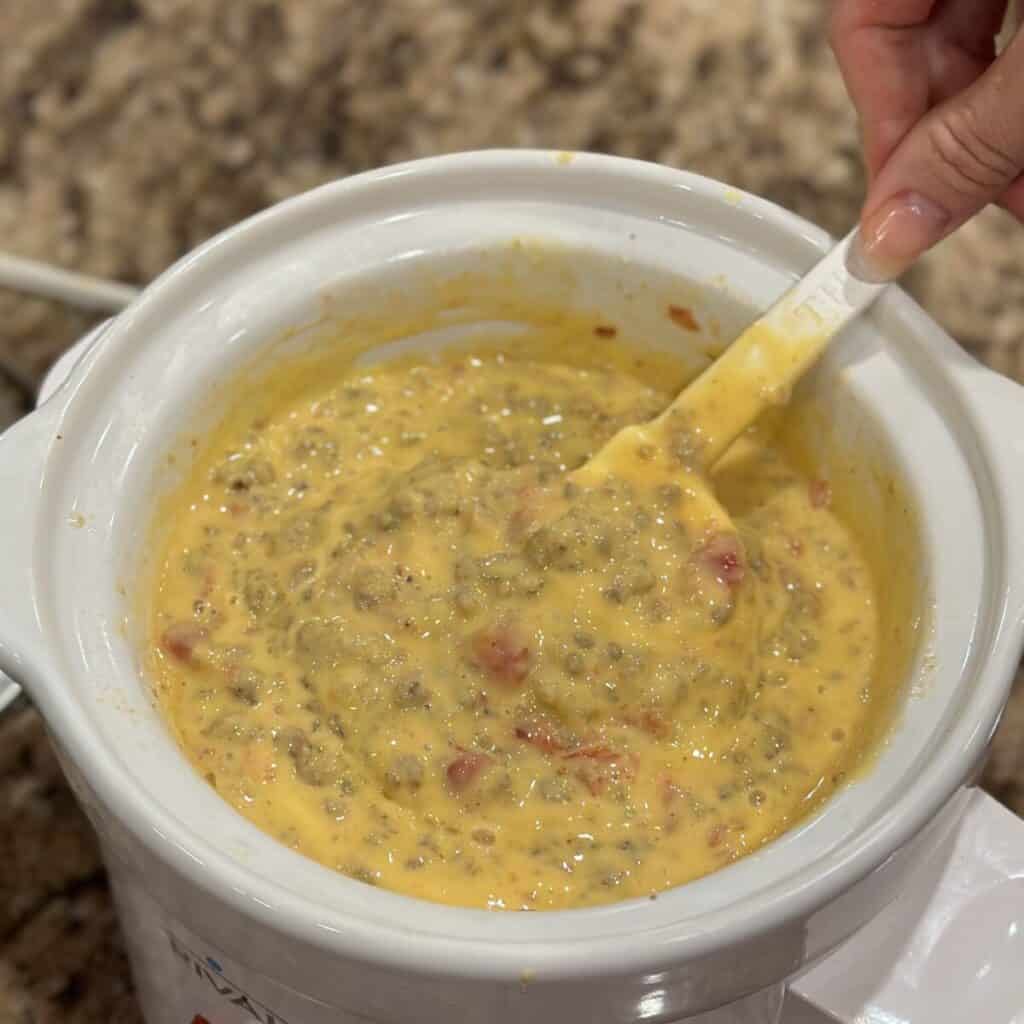 Stirring cheese and sausage dip in a crockpot.