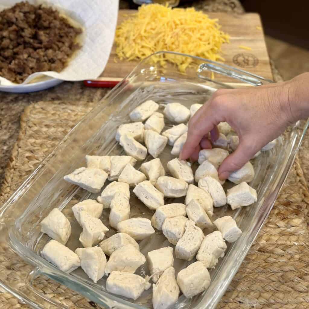 Assembling biscuits and gravy casserole in a baking dish.