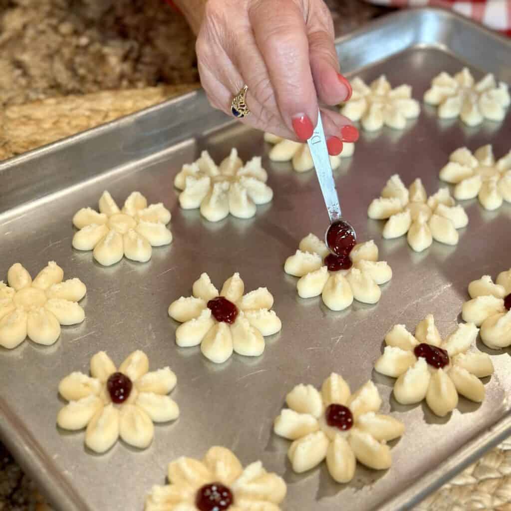 Pressing shortbread cookies on a sheet pan and adding jam to the middle.