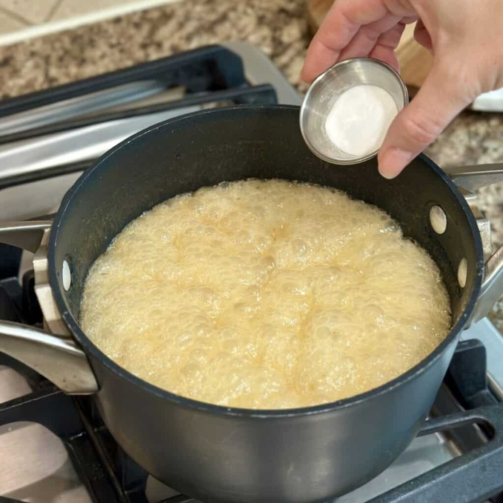 Adding baking soda to butter and sugar in a pan.