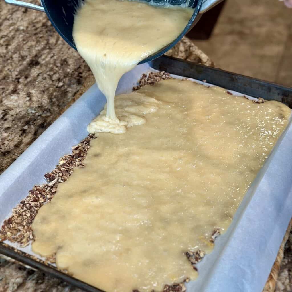 Adding toffee to the top of nuts on a sheet pan.