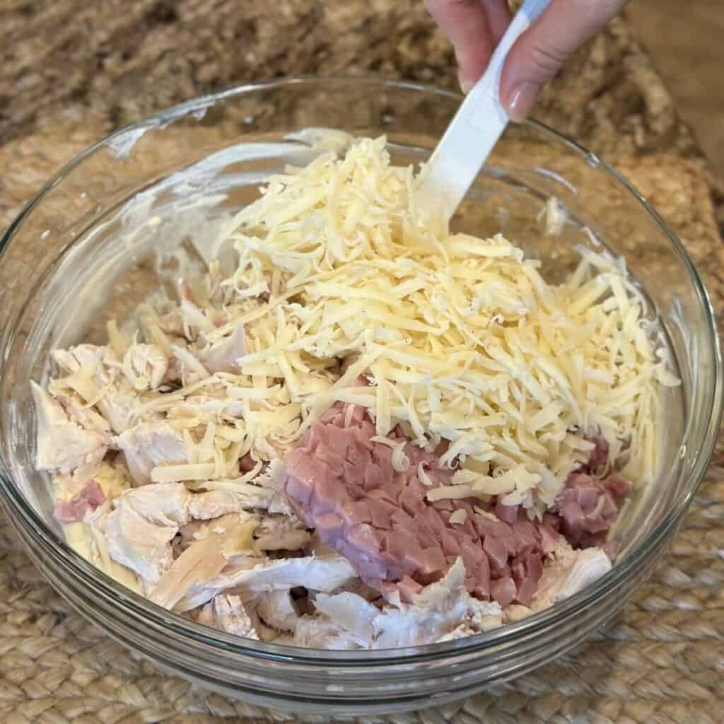 Mixing together the ingredients for chicken cordon bleu casserole in a bowl.