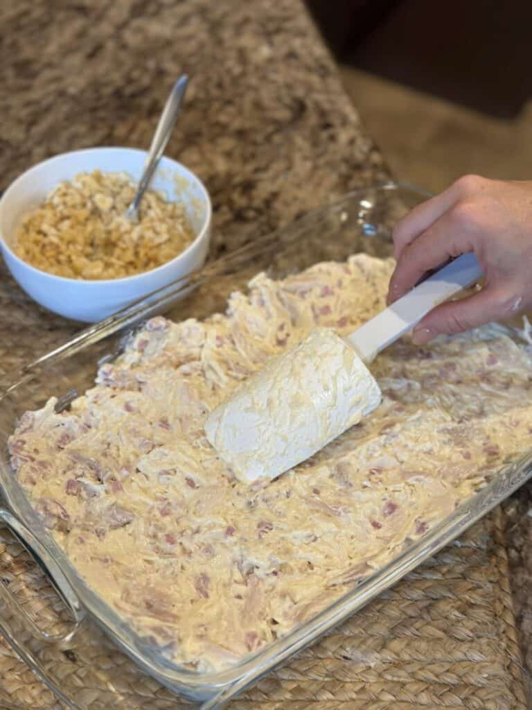 Spreading the filling for chicken cordon bleu casserole in a pan.