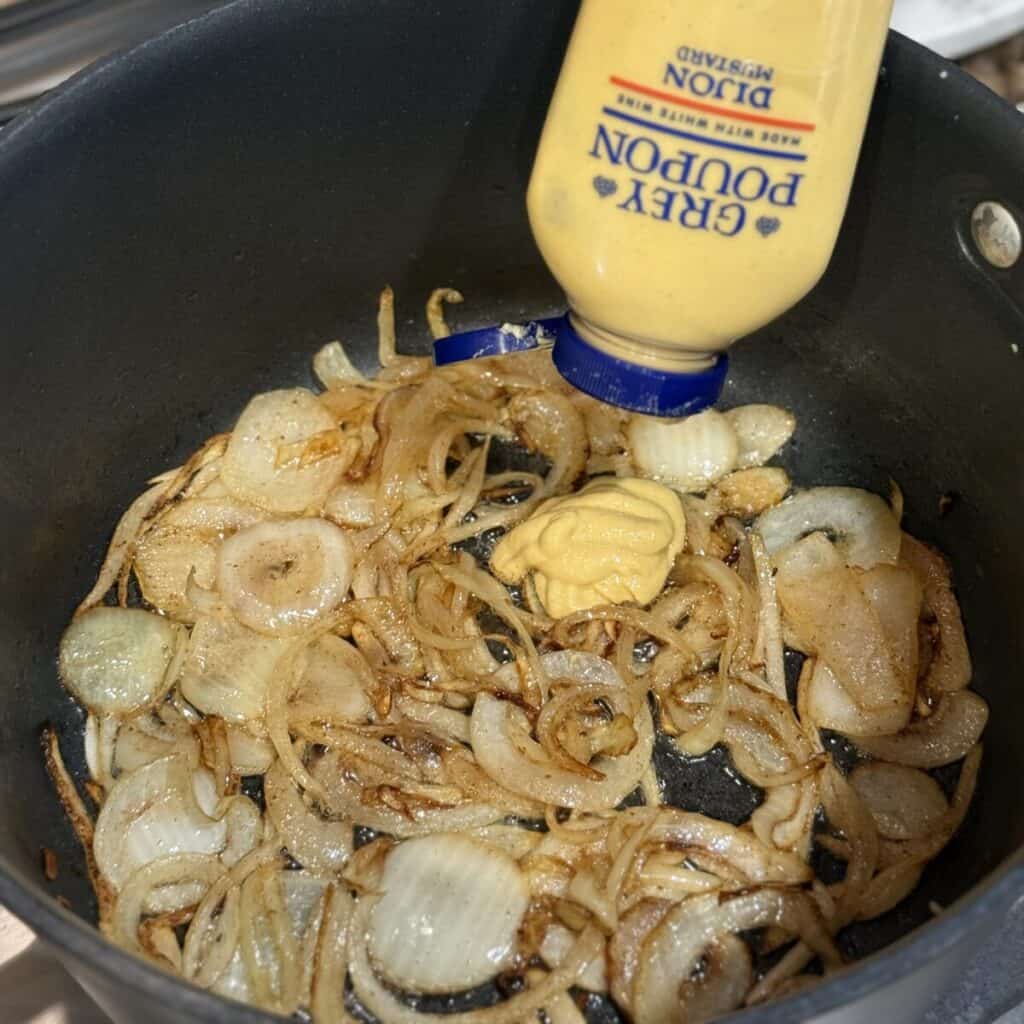 Adding dijon mustard to onions in a pan.