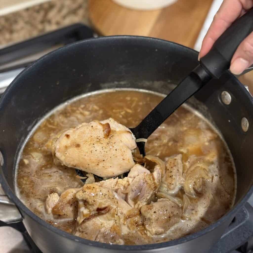 Adding chicken to broth in a pan.