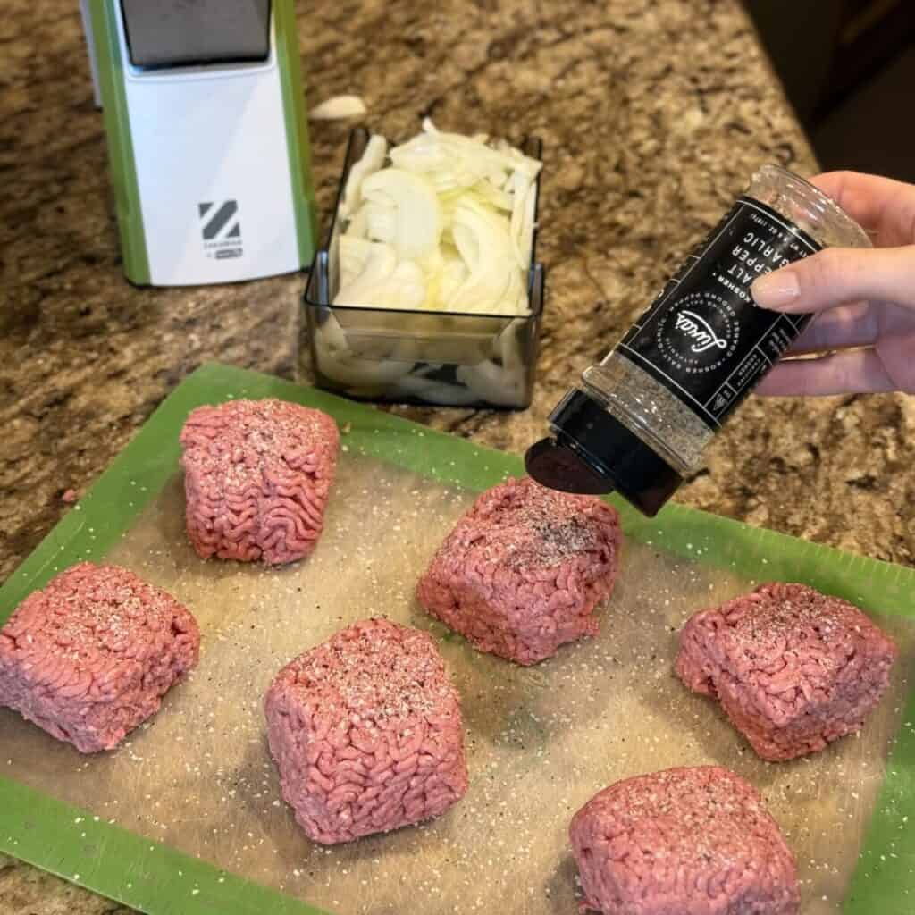 Seasoning ground beef on a cutting board.