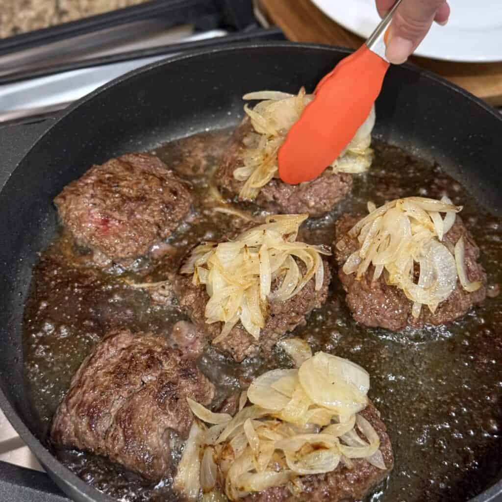 Adding onions and cheese to the top of hamburger steaks.